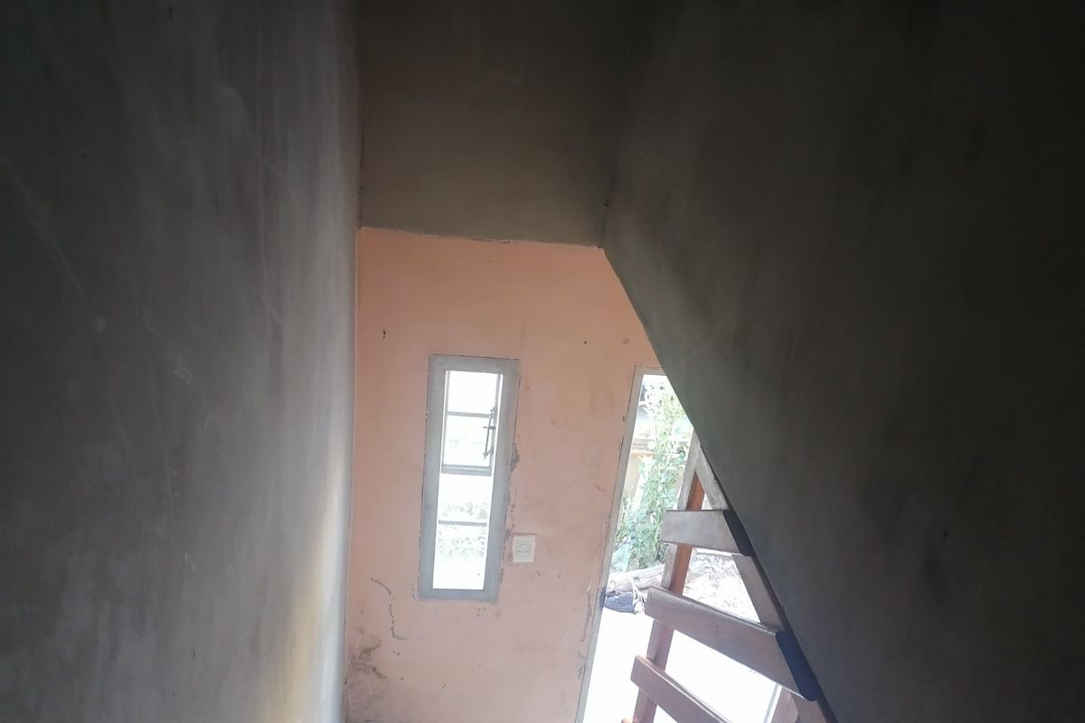 An unfinished interior hallway featuring exposed concrete walls and a wooden staircase, requiring significant finishing work to complete the space.