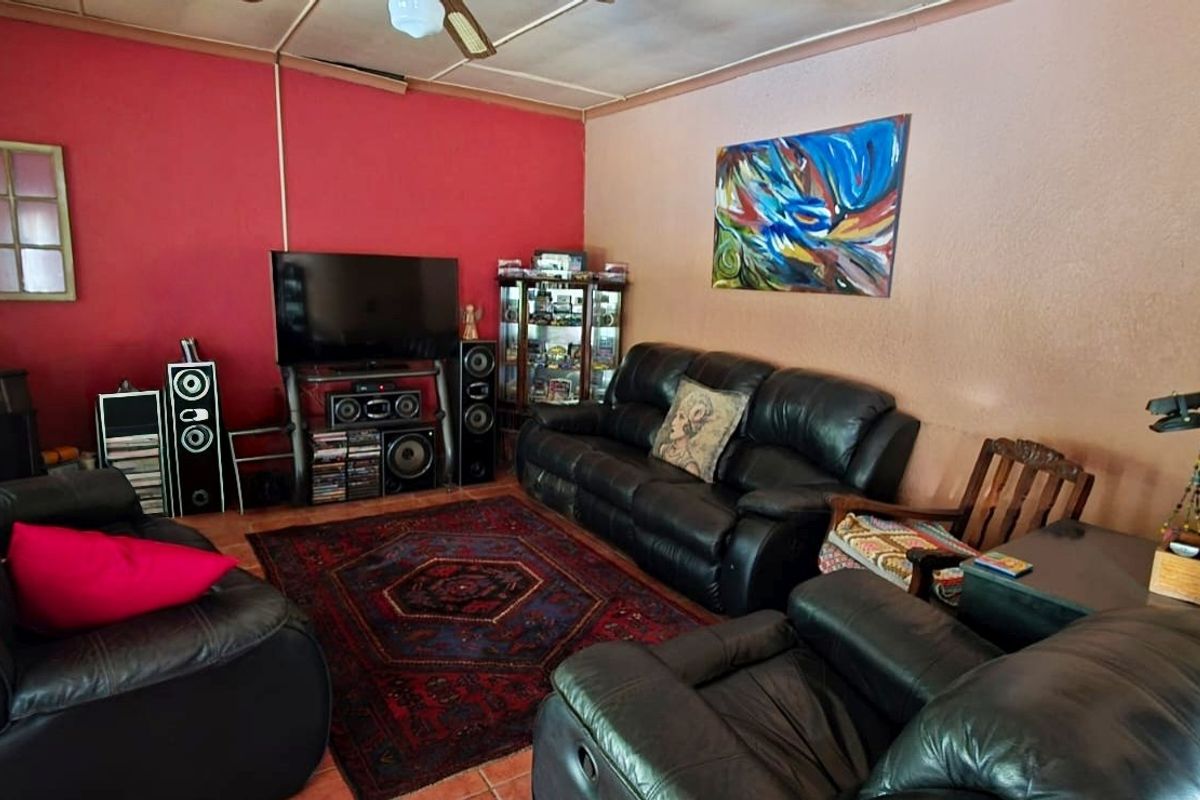A living room featuring tiled flooring and a ceiling fan, with dated wall finishes and visible ceiling paneling.