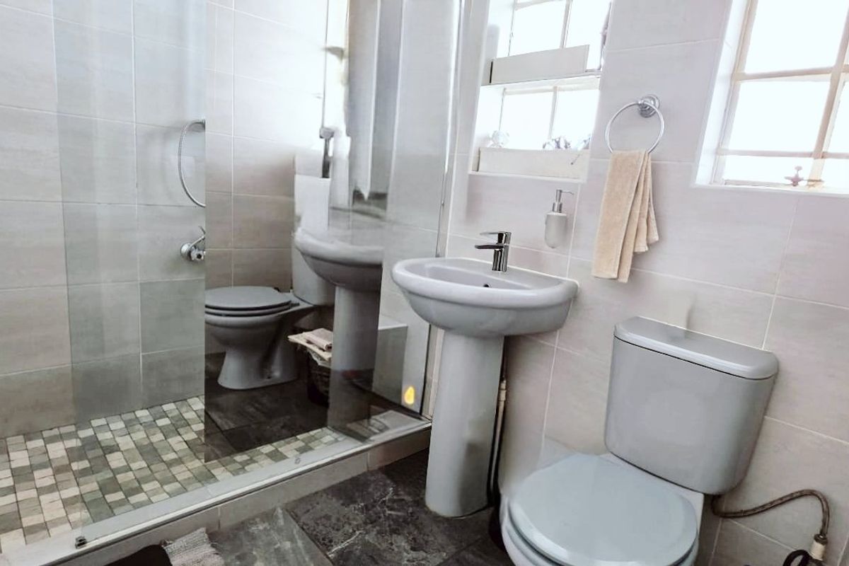 A functional bathroom featuring a pedestal basin, toilet, and a glass-enclosed shower with tiled finishes throughout.