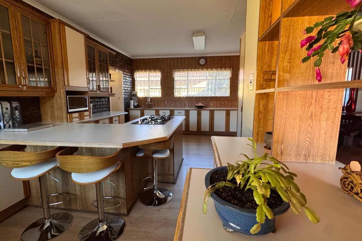 A spacious kitchen featuring wood-finish cabinetry, a central island with a gas hob, and exposed brick accents, offering a functional layout with ample storage.