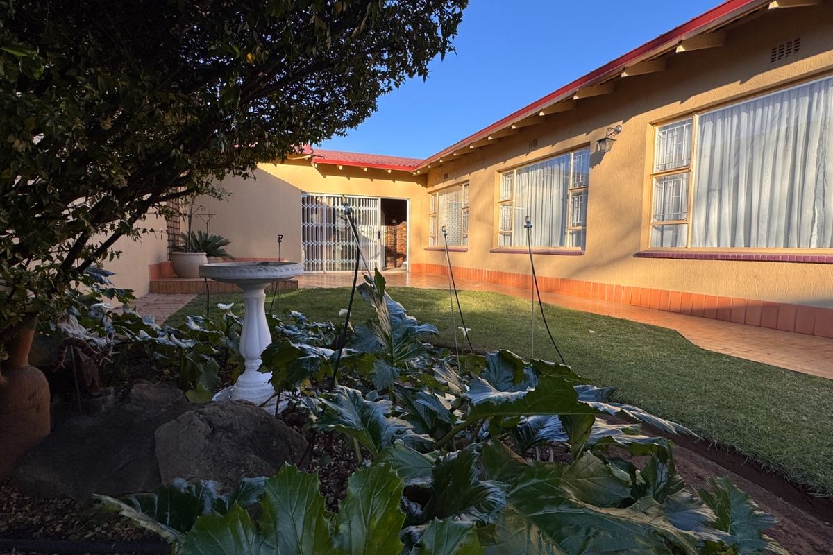 A well-maintained rear exterior view featuring a lawn, tiled patio area, and secure access point to the main house structure.