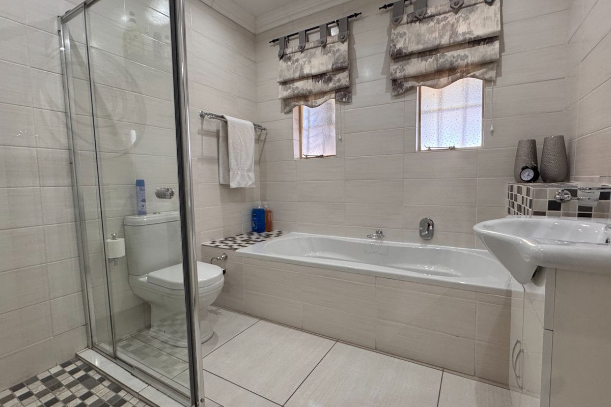 A well-maintained bathroom featuring a glass-enclosed shower, a built-in bathtub, neutral ceramic tiling, and modern fixtures.