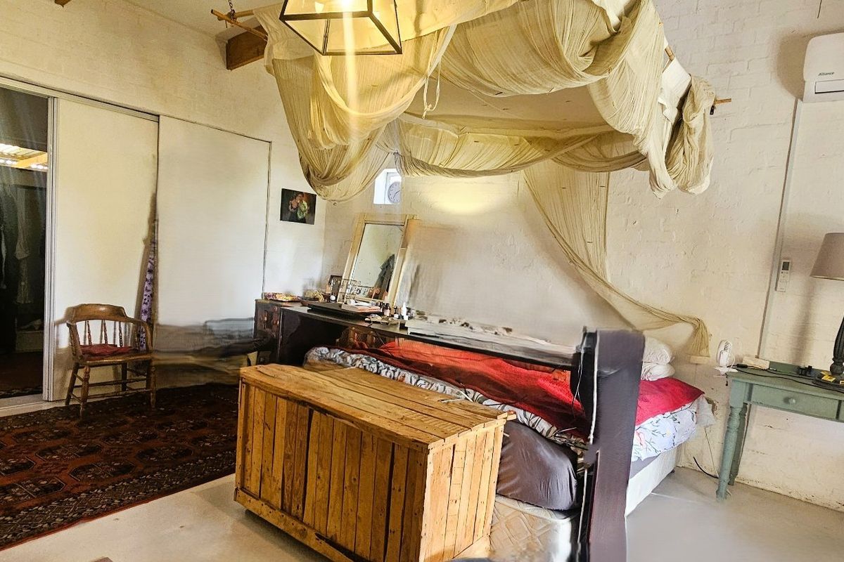 Spacious bedroom featuring painted brick walls, exposed timber ceiling beams, a split-system air conditioner, and a large sliding door wardrobe.