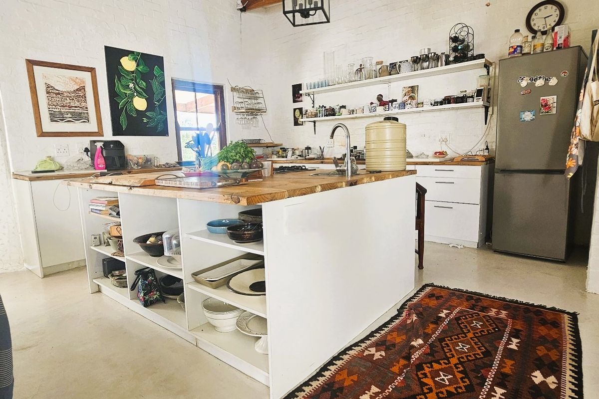 A rustic-style kitchen featuring a large central island with a timber countertop, open shelving, and exposed brick walls with timber ceiling beams.
