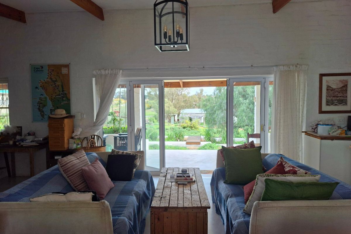Spacious living room featuring exposed timber ceiling beams, painted brick walls, and large sliding glass doors providing direct access to the outdoor patio and garden.
