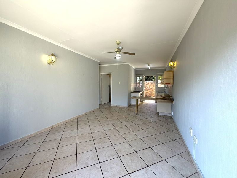 Open-plan living and kitchen area featuring tiled flooring, ceiling fan, wall sconces, and a functional kitchen layout with a breakfast bar.