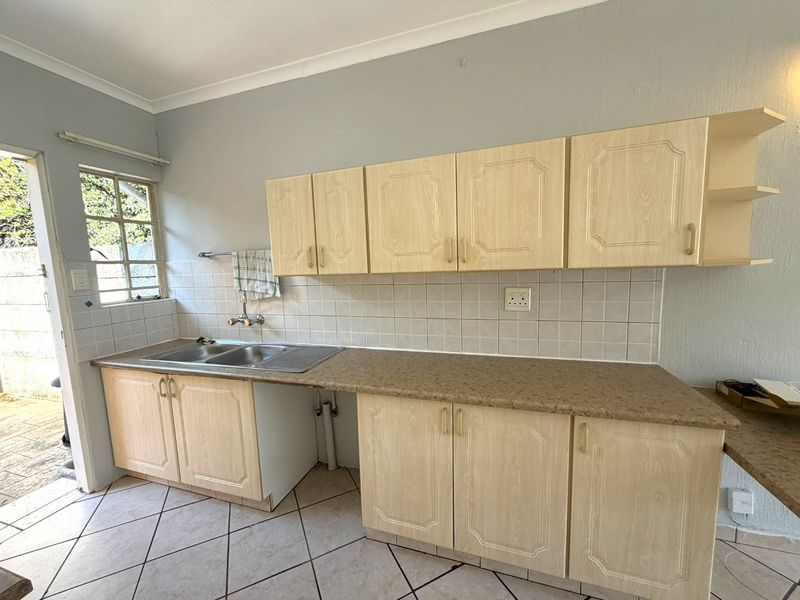 A functional kitchen featuring laminate cabinetry, a double bowl stainless steel sink, tiled backsplash, and ceramic flooring, offering potential for modernization.