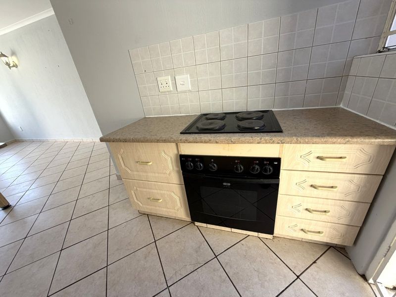A functional kitchen area featuring built-in cabinetry, an integrated electric oven and hob, tiled splashback, and durable ceramic floor tiles.