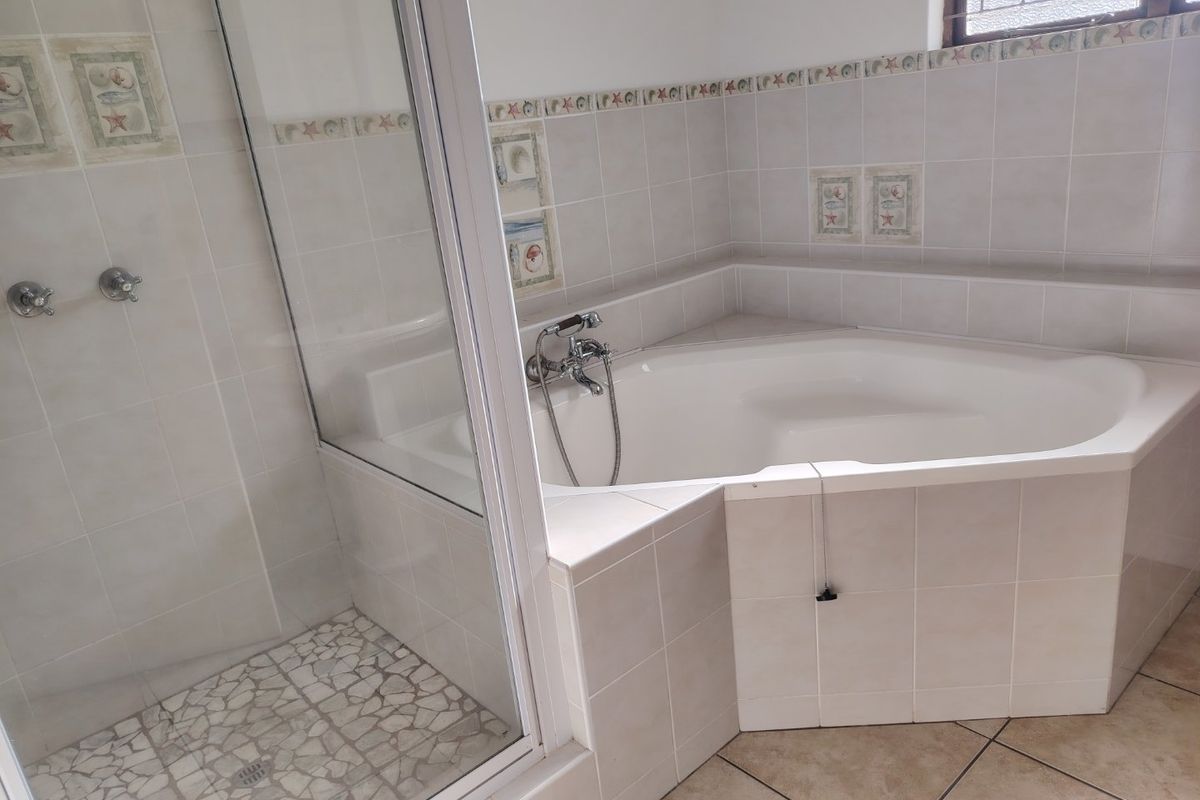 A functional bathroom featuring a corner bathtub, a separate glass-enclosed shower, and neutral ceramic tiling throughout.