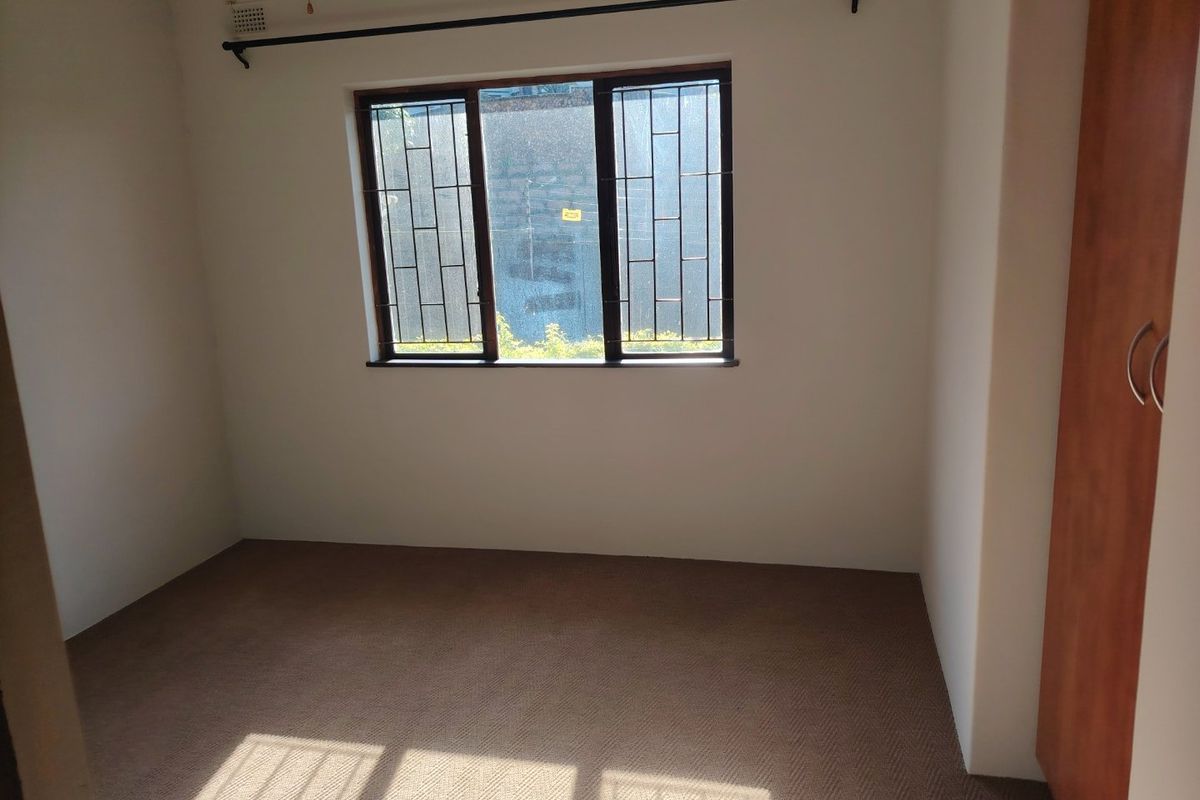 An empty bedroom featuring neutral carpet flooring, a built-in wardrobe, and a window fitted with security bars.