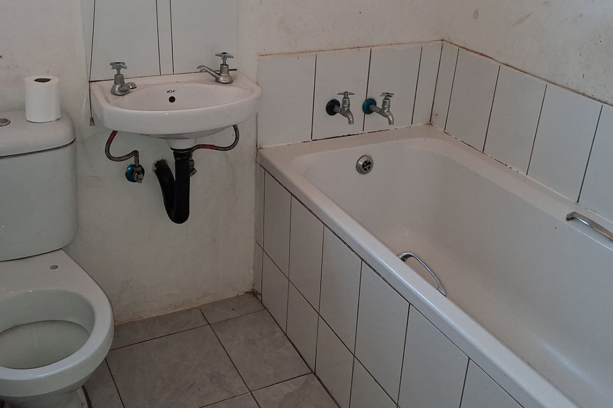 A functional bathroom featuring a standard bathtub, wall-mounted basin, and toilet with tiled finishes, currently requiring cosmetic updates and maintenance.