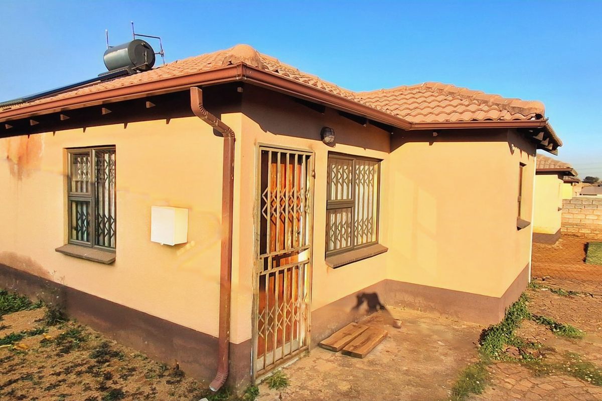 Rear exterior view of a single-story house featuring a tiled roof, solar water heater, and security bars on windows and doors.