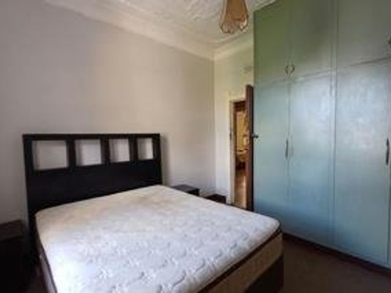 A bedroom featuring built-in cupboards and ornate ceiling detailing, offering a functional space with potential for cosmetic updates.