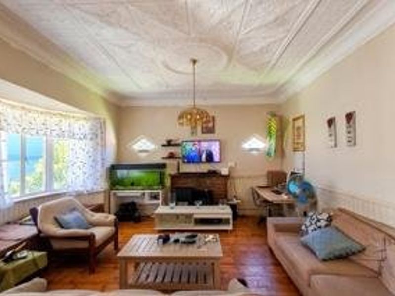 Spacious living room featuring an ornate plaster ceiling, hardwood flooring, wainscoting, and a large bay window providing natural light.