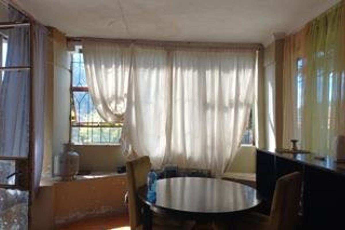 A living area featuring large windows with security bars, showing signs of wear on the walls and requiring cosmetic updates.