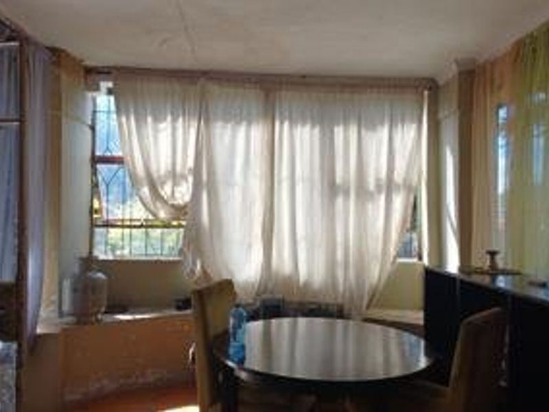 A living area featuring large windows with security bars, showing signs of wear on the walls and requiring cosmetic updates.