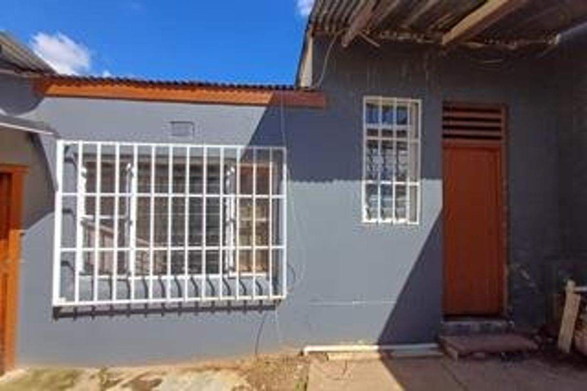 Rear exterior view of the property featuring a painted wall, security bars on the window, and a timber door with corrugated roofing.