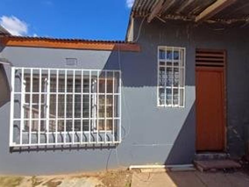 Rear exterior view of the property featuring a painted wall, security bars on the window, and a timber door with corrugated roofing.