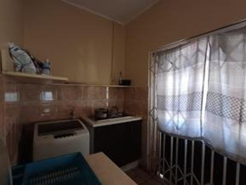 A functional laundry area featuring built-in cabinetry, tiled splashbacks, and a security gate over the window, offering a practical utility space.