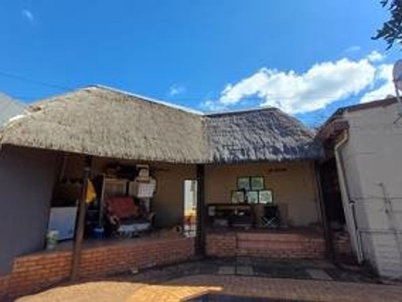 A covered outdoor patio area featuring a traditional thatched roof and brick foundation, providing a rustic space for outdoor living.