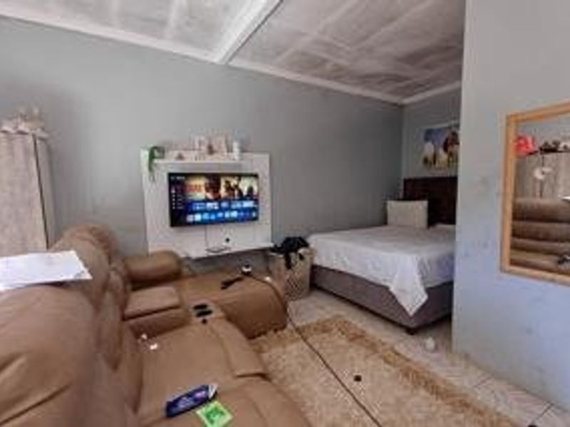 A bedroom featuring tiled flooring and a built-in media unit, showing signs of wear on the ceiling and walls.