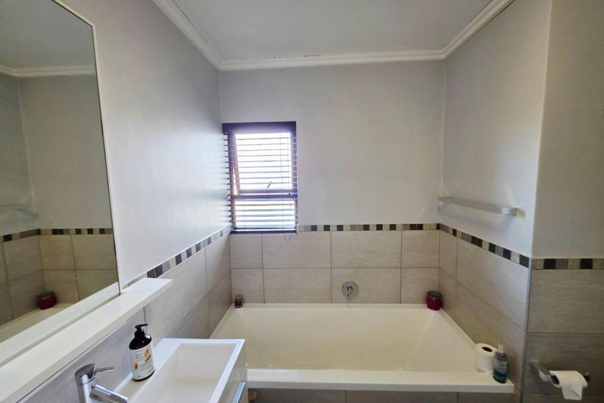 A clean and functional bathroom featuring a built-in bathtub, wall-mounted basin with mixer tap, and neutral wall tiling with a decorative border.