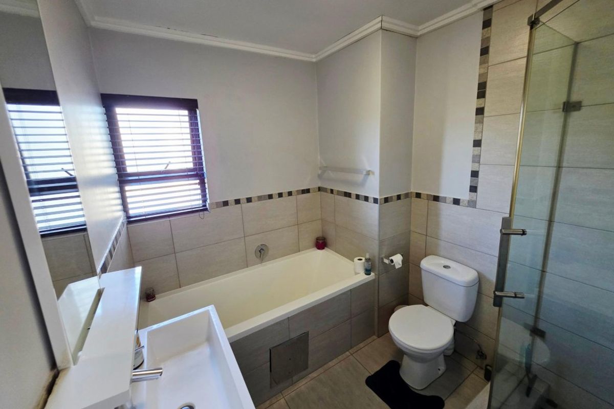 A functional bathroom featuring a bathtub, separate glass shower enclosure, toilet, and basin with neutral wall and floor tiling.
