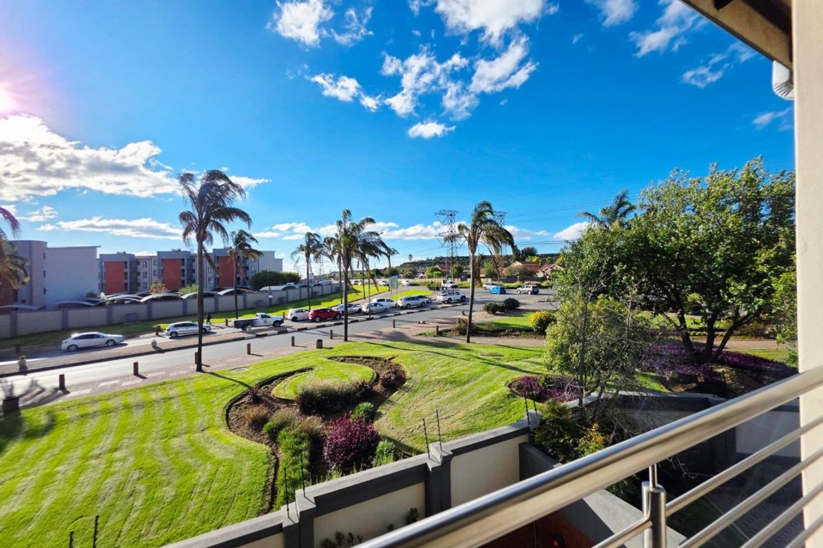 Elevated view from a balcony overlooking a landscaped garden, street, and surrounding residential area.
