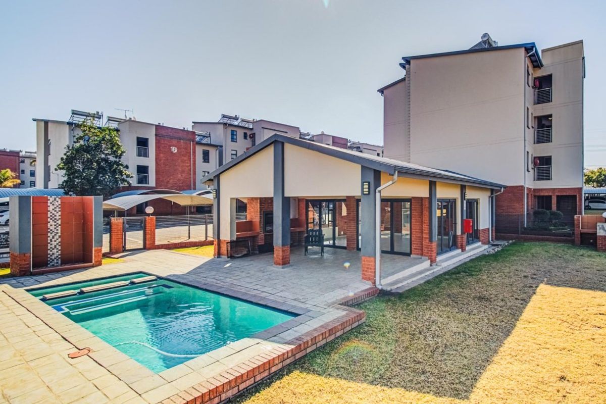Communal pool area featuring a covered patio with built-in braai facilities, brick paving, and direct access to the apartment complex grounds.