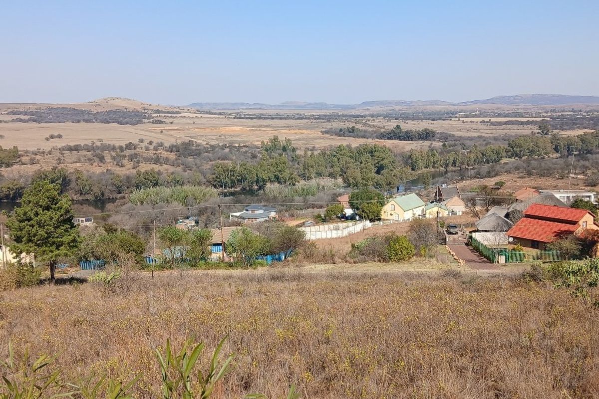 A wide-angle view overlooking a rural landscape with scattered residential properties, natural vegetation, and distant hills.