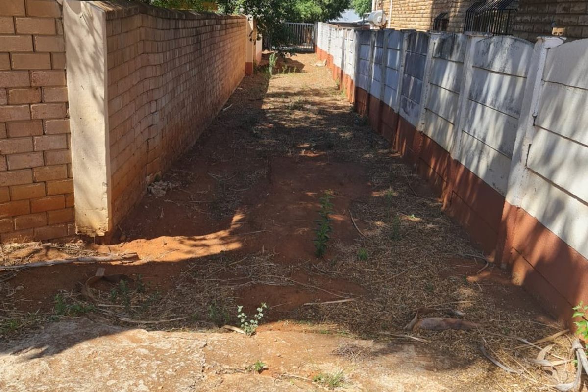 A narrow side passage between two boundary walls featuring a concrete apron and unlandscaped earth ground.