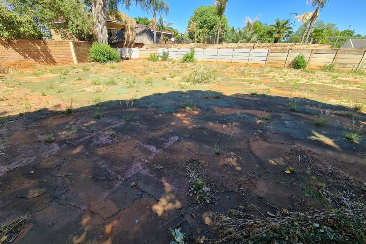 A spacious rear yard area featuring perimeter brick and concrete walling with extensive paved surfaces requiring maintenance and landscaping.