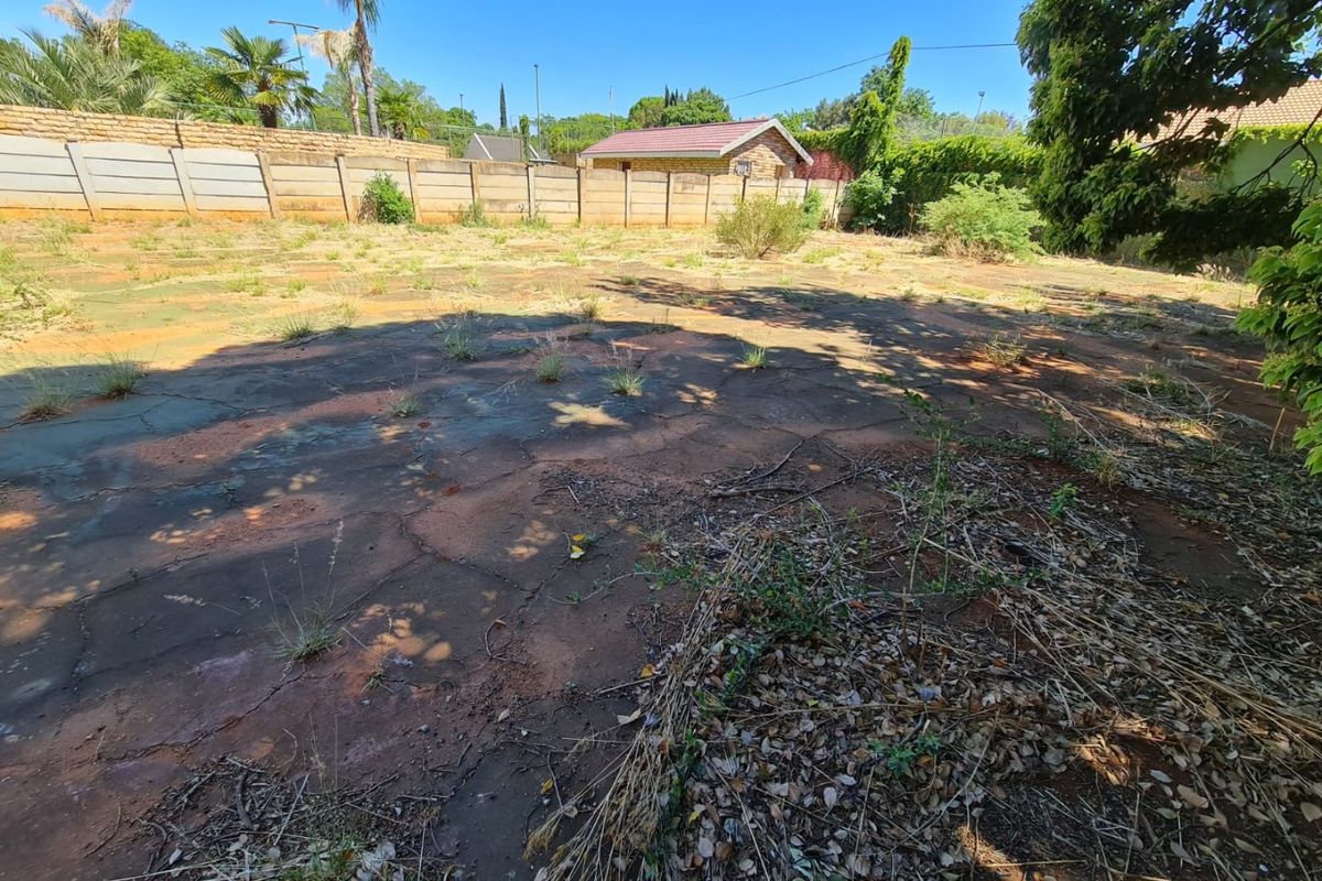 A vacant residential plot featuring a weathered paved area and a precast concrete boundary wall, requiring significant landscaping and site preparation.