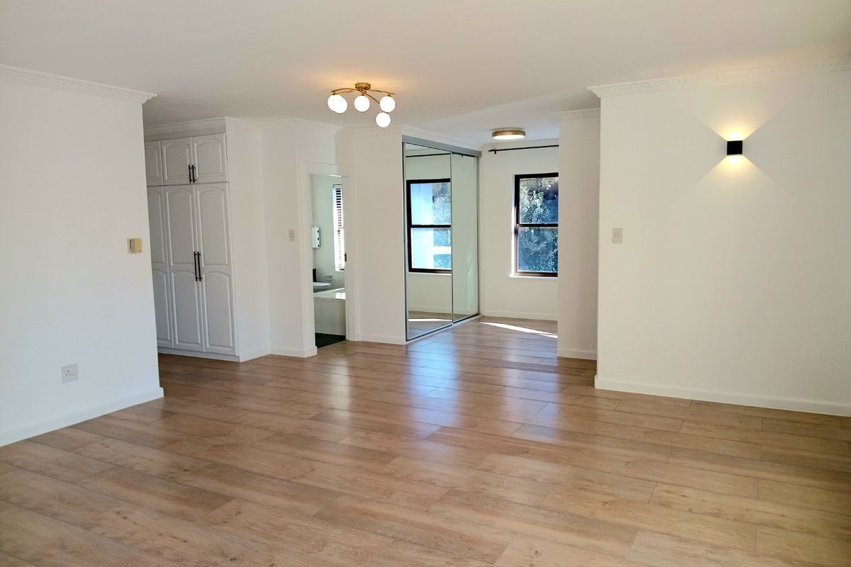 Spacious, light-filled bedroom featuring wood-look tile flooring, built-in cupboards with mirrored doors, and modern lighting fixtures.