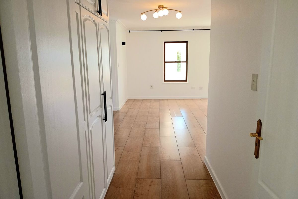 A bright, empty living area featuring wood-look tiled flooring, built-in storage cabinetry, and a modern ceiling light fixture.