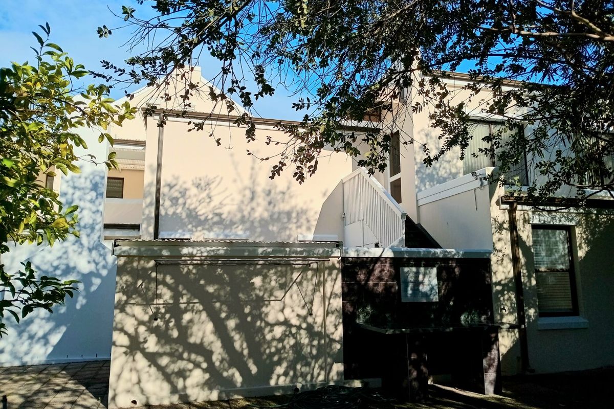 Rear exterior view of the property featuring a paved patio area, built-in braai, and an external staircase leading to the upper level.