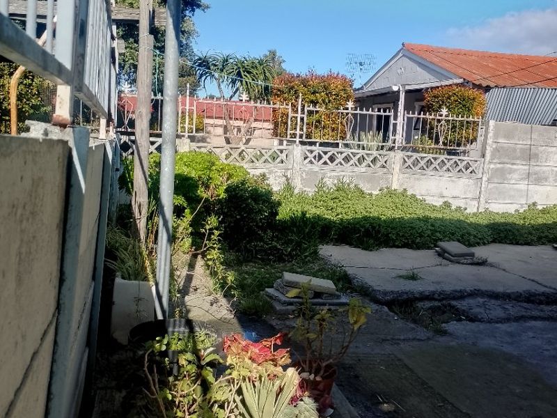 Rear outdoor area featuring a concrete patio, metal security fencing, and a boundary wall, offering potential for landscaping and outdoor improvement.