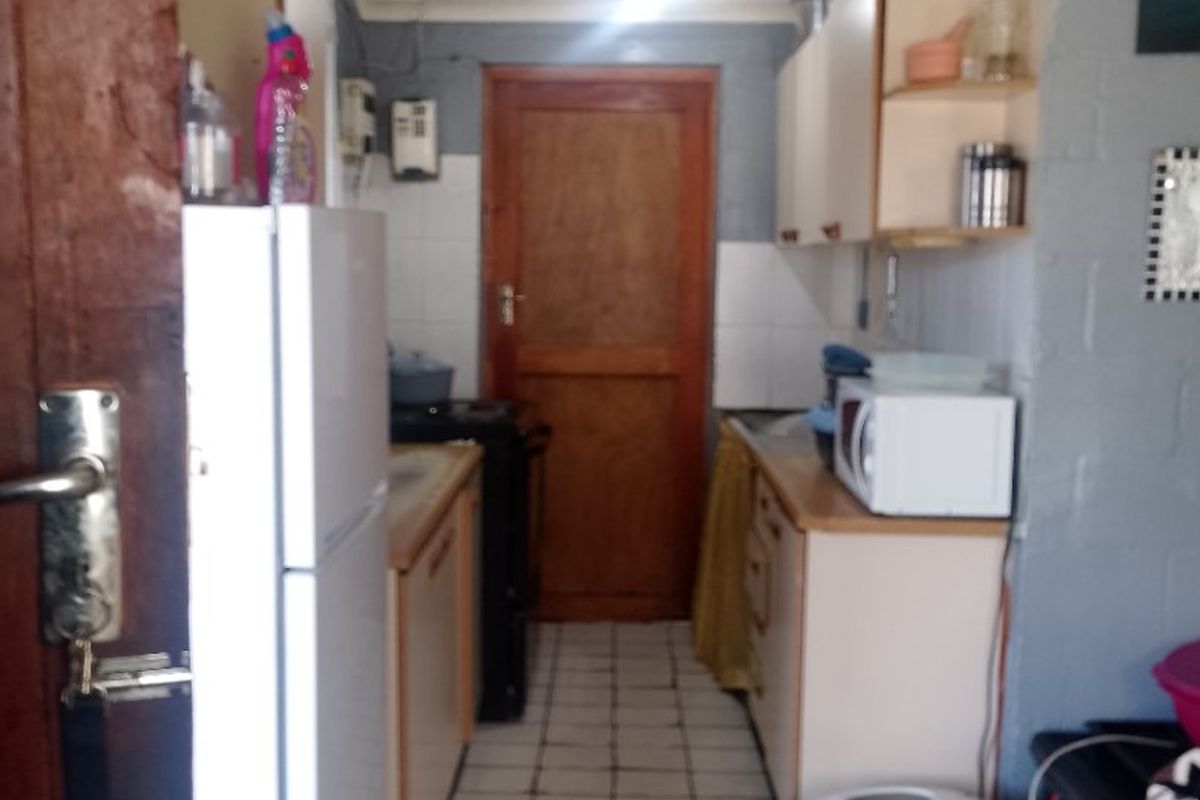 A compact kitchen featuring tiled flooring, fitted cabinetry, and a timber door, offering a functional layout in need of cosmetic updates.