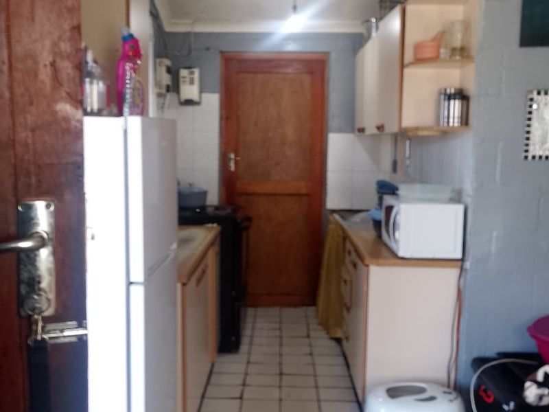 A compact kitchen featuring tiled flooring, fitted cabinetry, and a timber door, offering a functional layout in need of cosmetic updates.