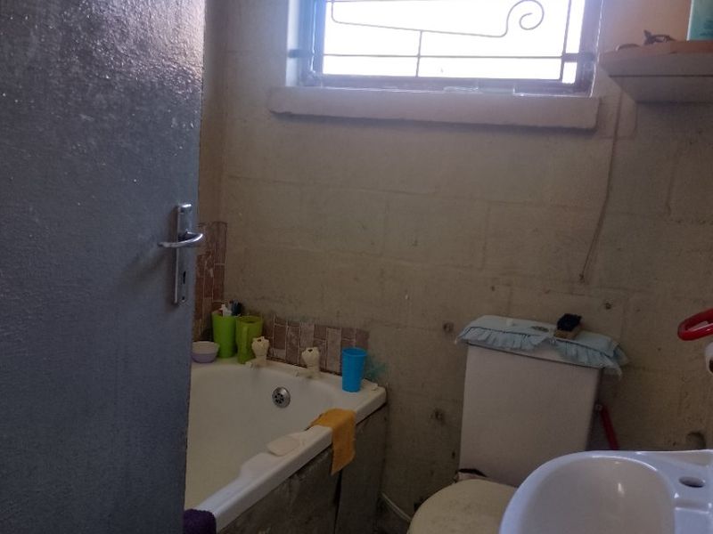 A compact bathroom featuring a bathtub, toilet, and pedestal basin, requiring cosmetic updates and finishing to improve its overall condition and aesthetic appeal.