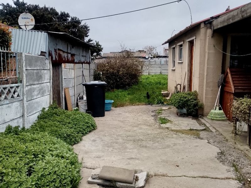 Rear exterior area featuring cracked concrete paving, a precast boundary wall, and a structure with a corrugated metal roof.