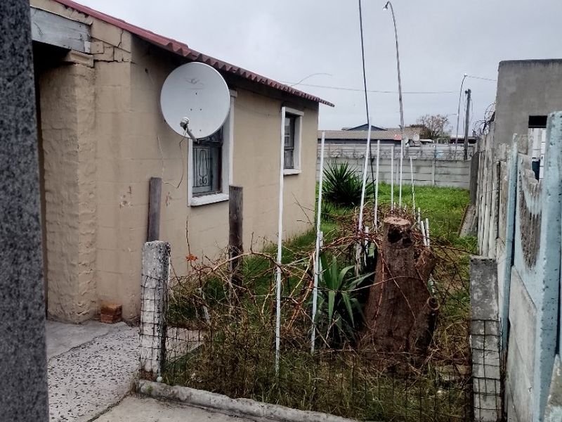 Rear exterior view of the property showing a concrete boundary wall, paved area, and exterior wall with a satellite dish.