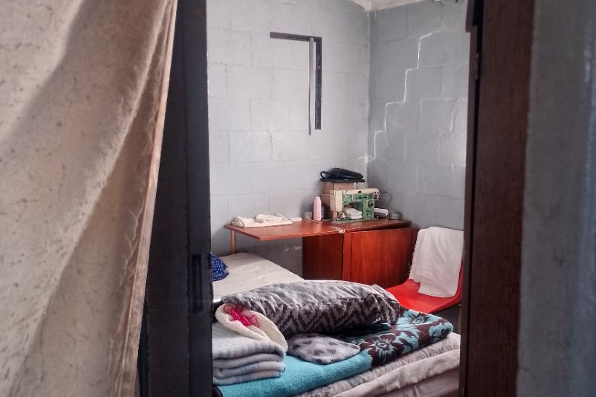 A small bedroom featuring exposed concrete block walls and a simple pendant light fixture, requiring cosmetic updates to improve the overall finish.
