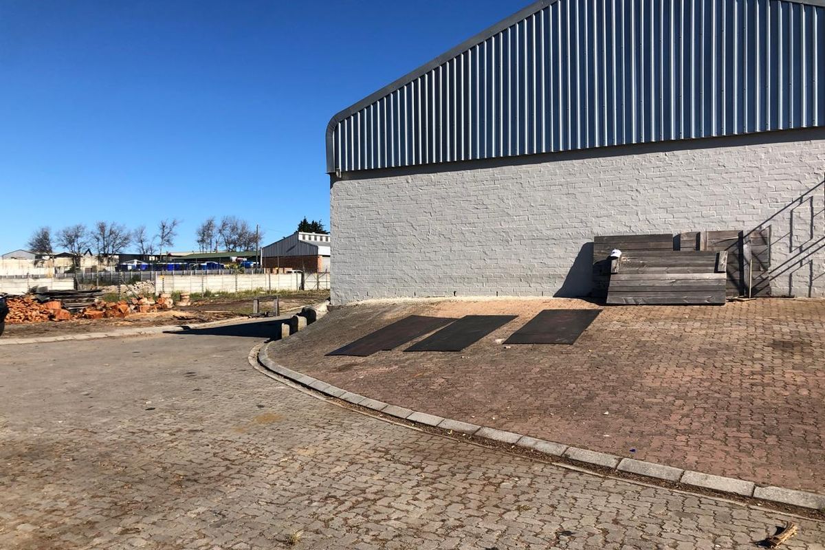 Exterior view of an industrial warehouse building featuring a painted brick facade, corrugated metal roof, and paved yard area.