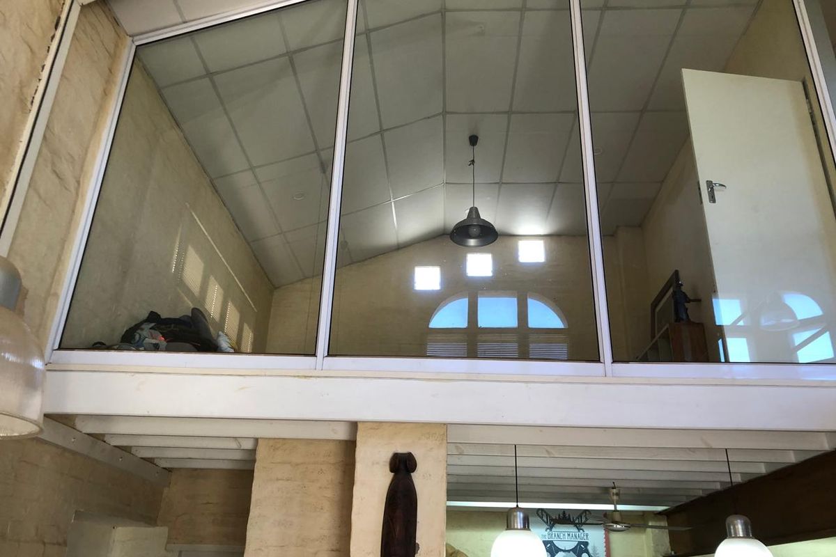 A mezzanine level office space featuring glass partitioning, suspended ceilings, and exposed brickwork, providing an open and industrial aesthetic.