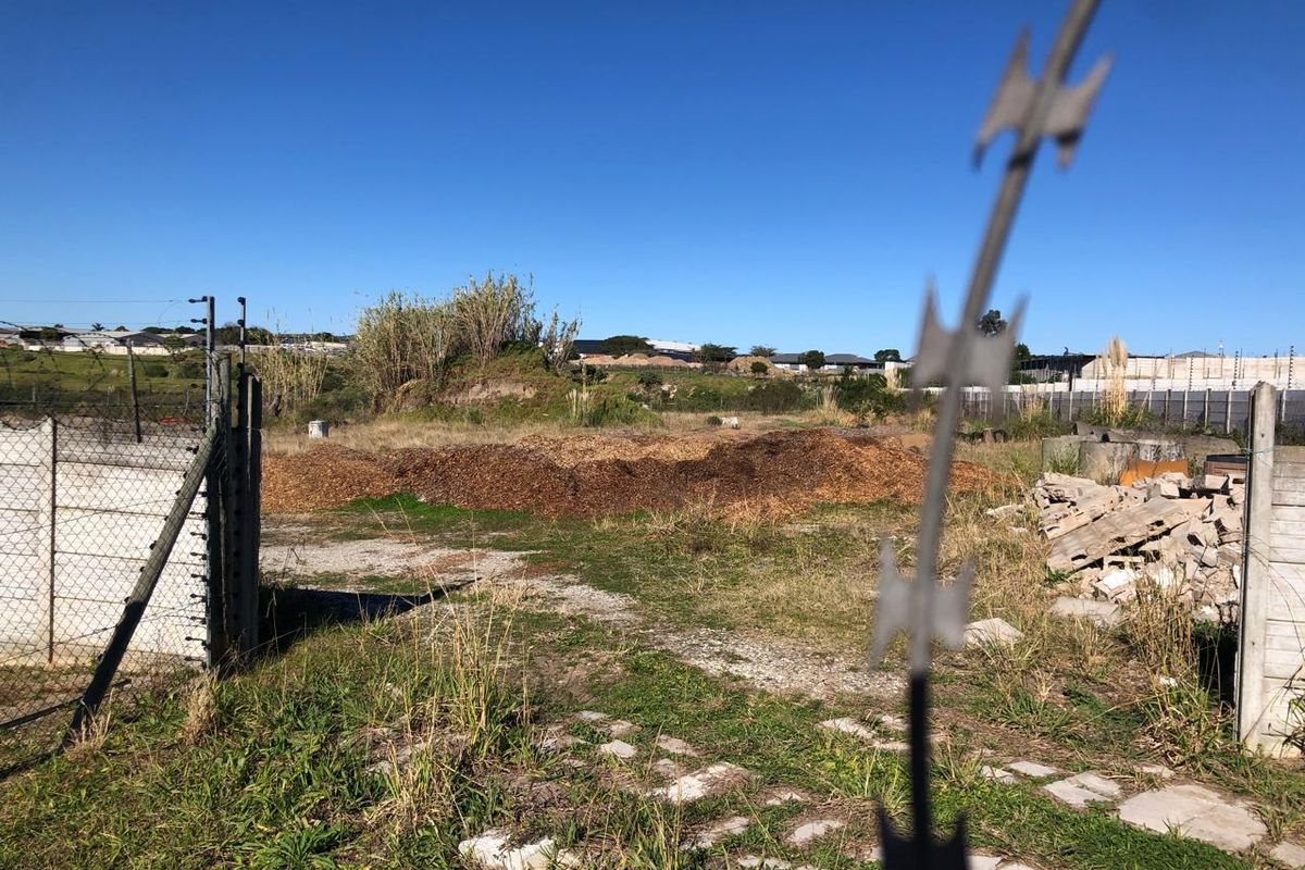 An industrial outdoor yard area featuring perimeter chain link and razor wire fencing, with visible debris and overgrown ground cover.