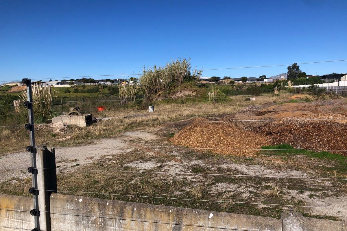 An undeveloped industrial plot featuring a concrete boundary wall and electric fencing, with natural vegetation and cleared ground areas.