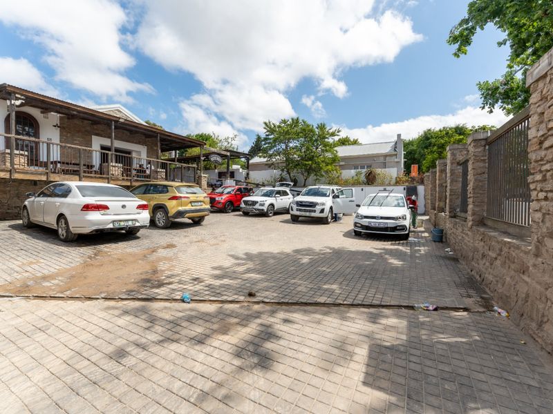 A paved commercial parking area featuring a stone boundary wall and a covered veranda attached to the main building structure.