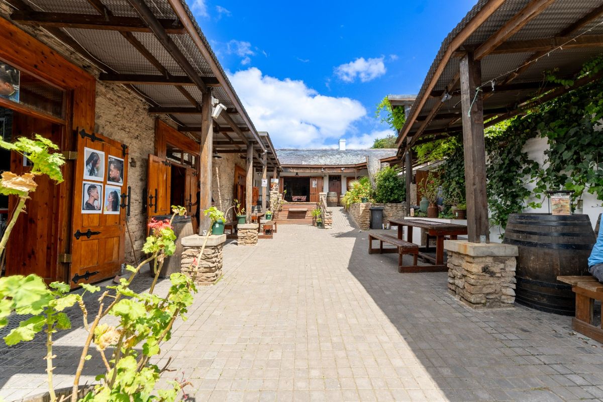 A charming rustic courtyard featuring stone masonry walls, timber pergolas, and paved walkways, creating an inviting outdoor commercial or hospitality space.