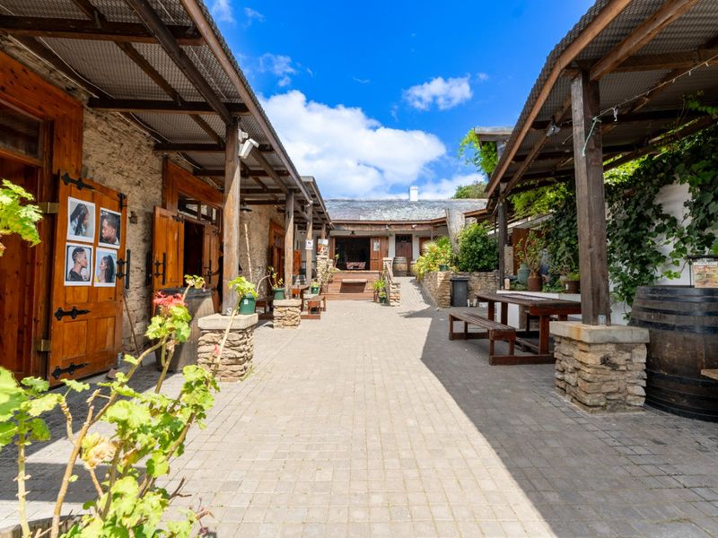 A charming rustic courtyard featuring stone masonry walls, timber pergolas, and paved walkways, creating an inviting outdoor commercial or hospitality space.
